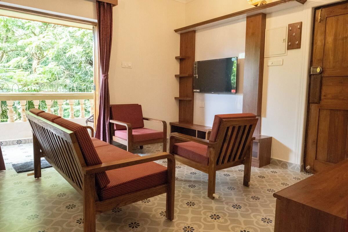 Une pièce avec un banc en bois, deux chaises rouges, un téléviseur fixé au mur et une porte en bois.