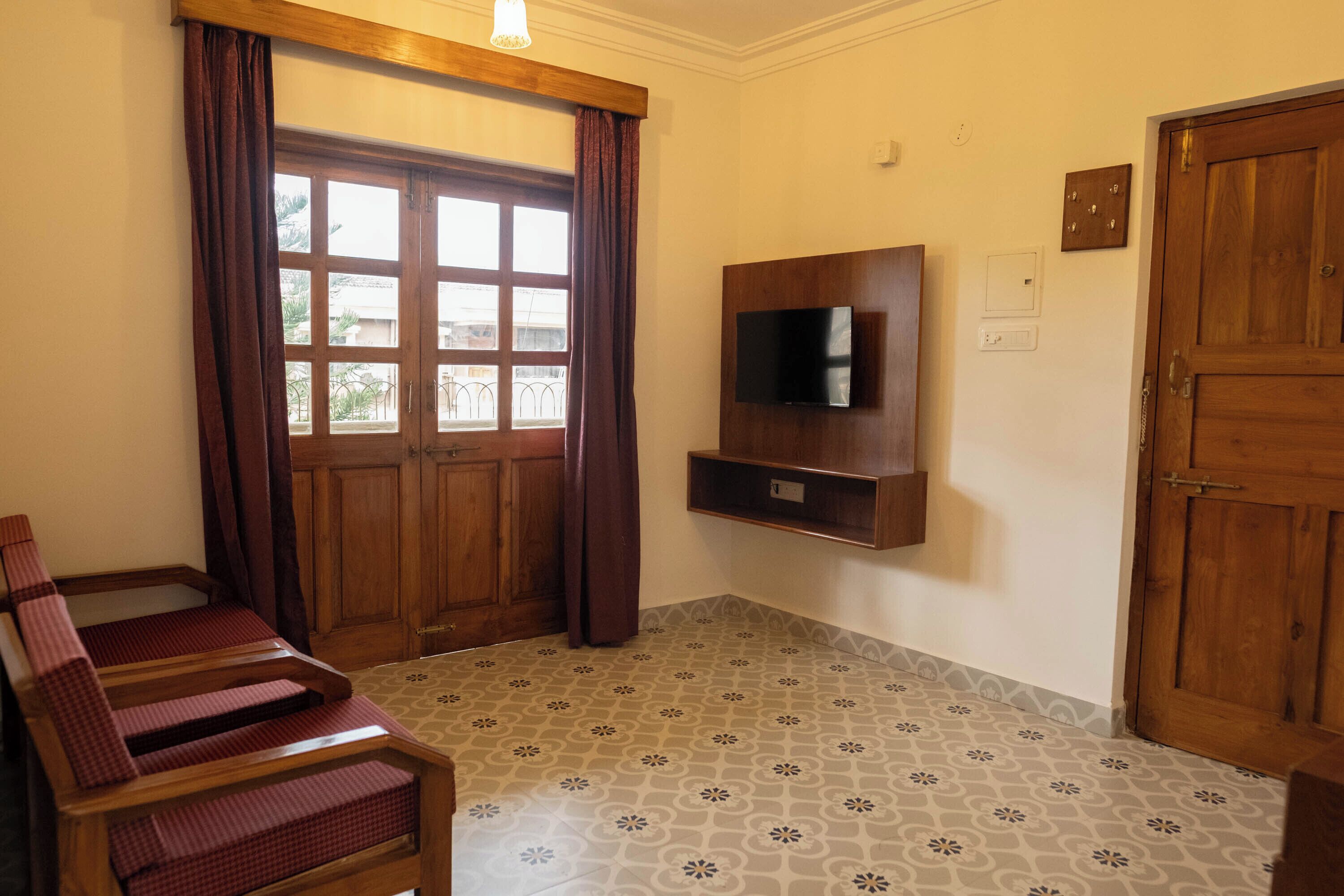 Une pièce avec une chaise en bois, un téléviseur fixé au mur, une porte en bois et des carreaux de sol à motifs.