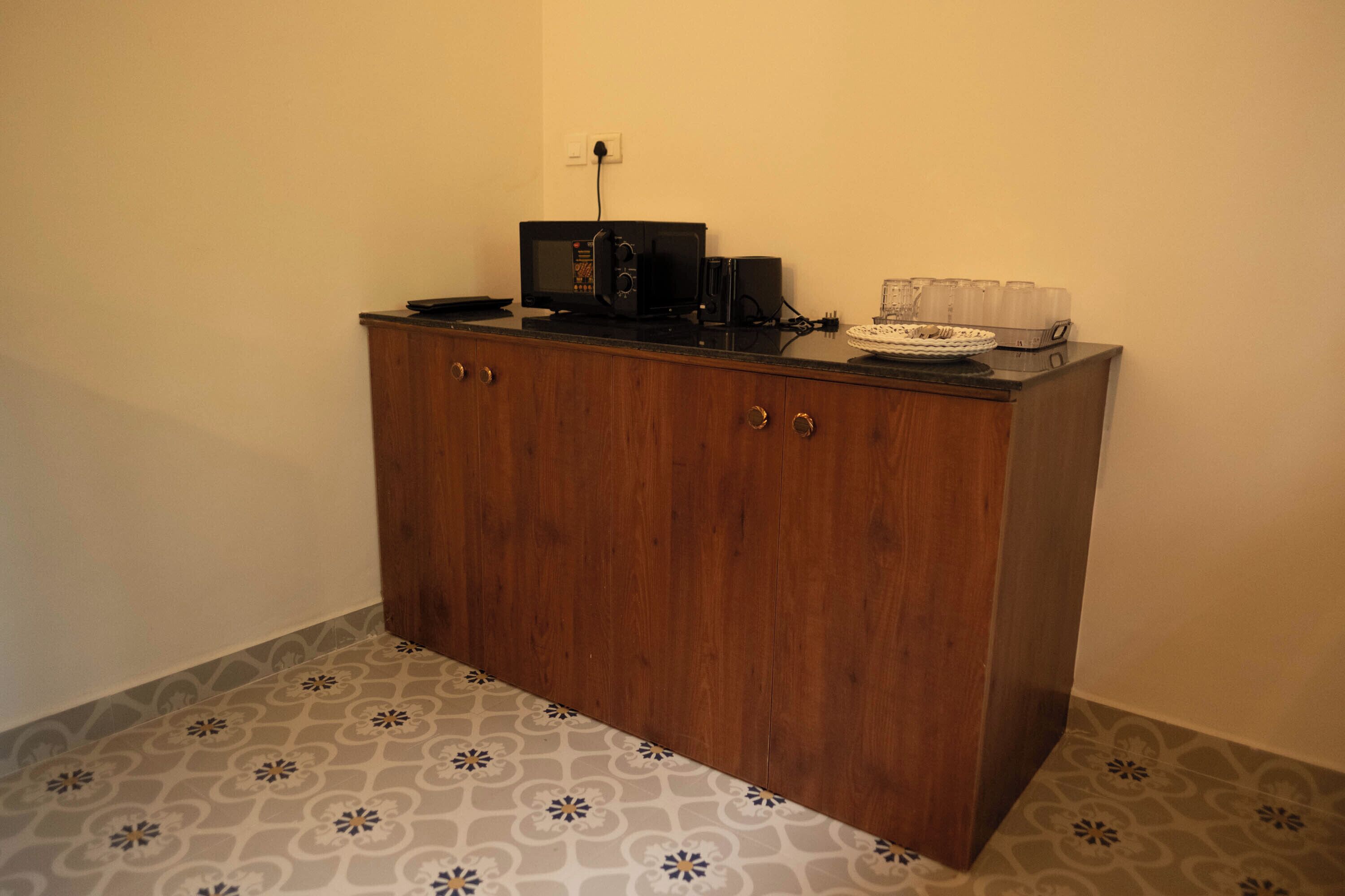 A wooden cabinet with a microwave and a coffee maker on top, a patterned floor, and a power outlet on the wall.