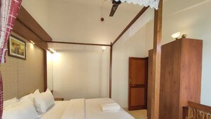 A bedroom with a large bed, wooden wardrobe, and a ceiling fan. - VISTAR HOLIDAYS (Candolim)