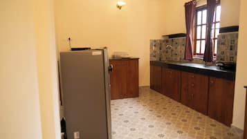 A compact kitchen with a refrigerator, wooden cabinets, a tiled backsplash, and a window with curtains.