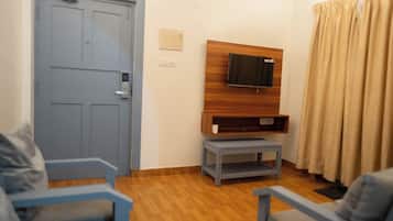 Ein Zimmer mit einer blauen Tür, einem an einer Holzplatte montierten Fernseher, einem kleinen grauen Tisch und einem grauen Sofa.