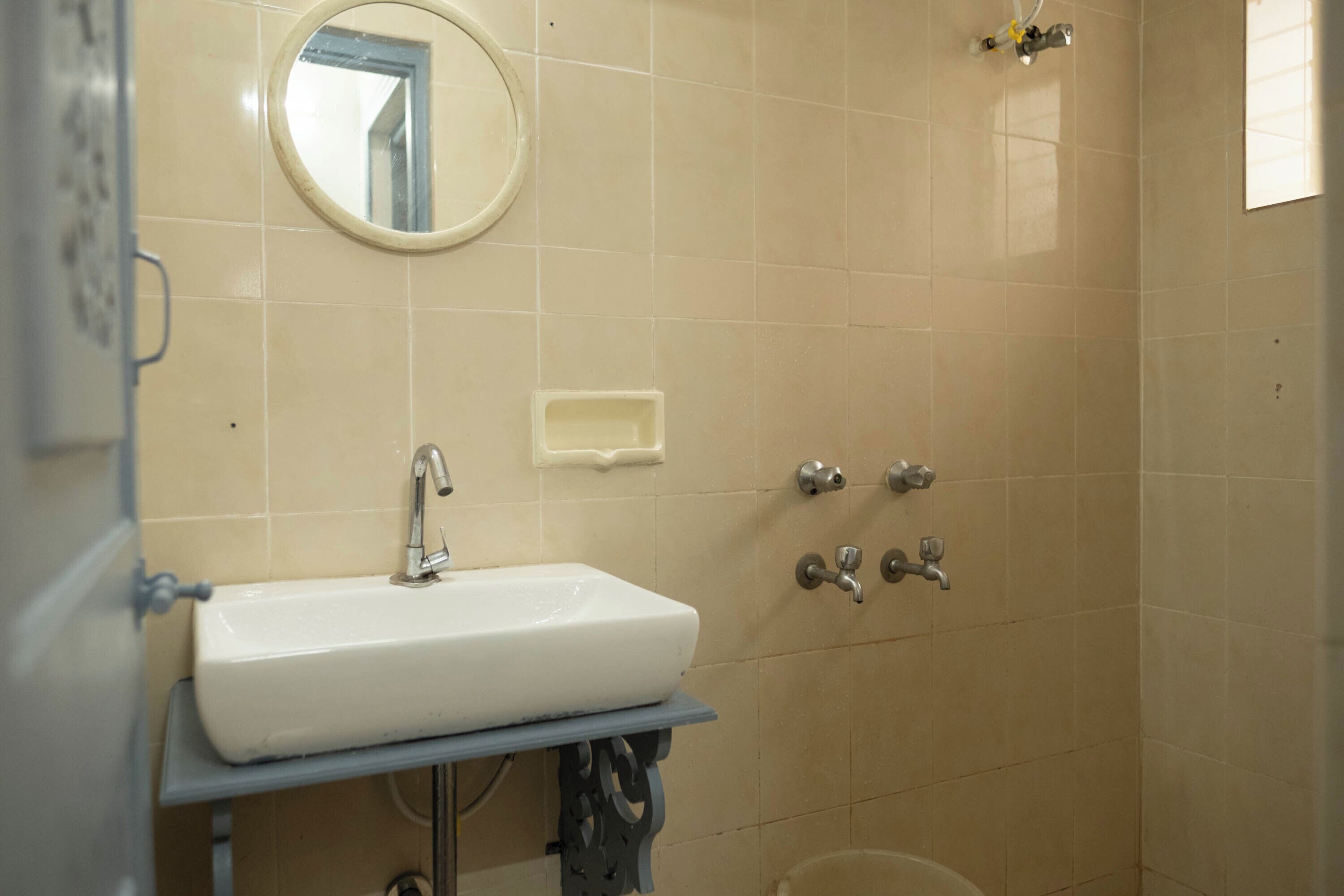 A bathroom with a white sink, a round mirror, and a shower with multiple faucets.