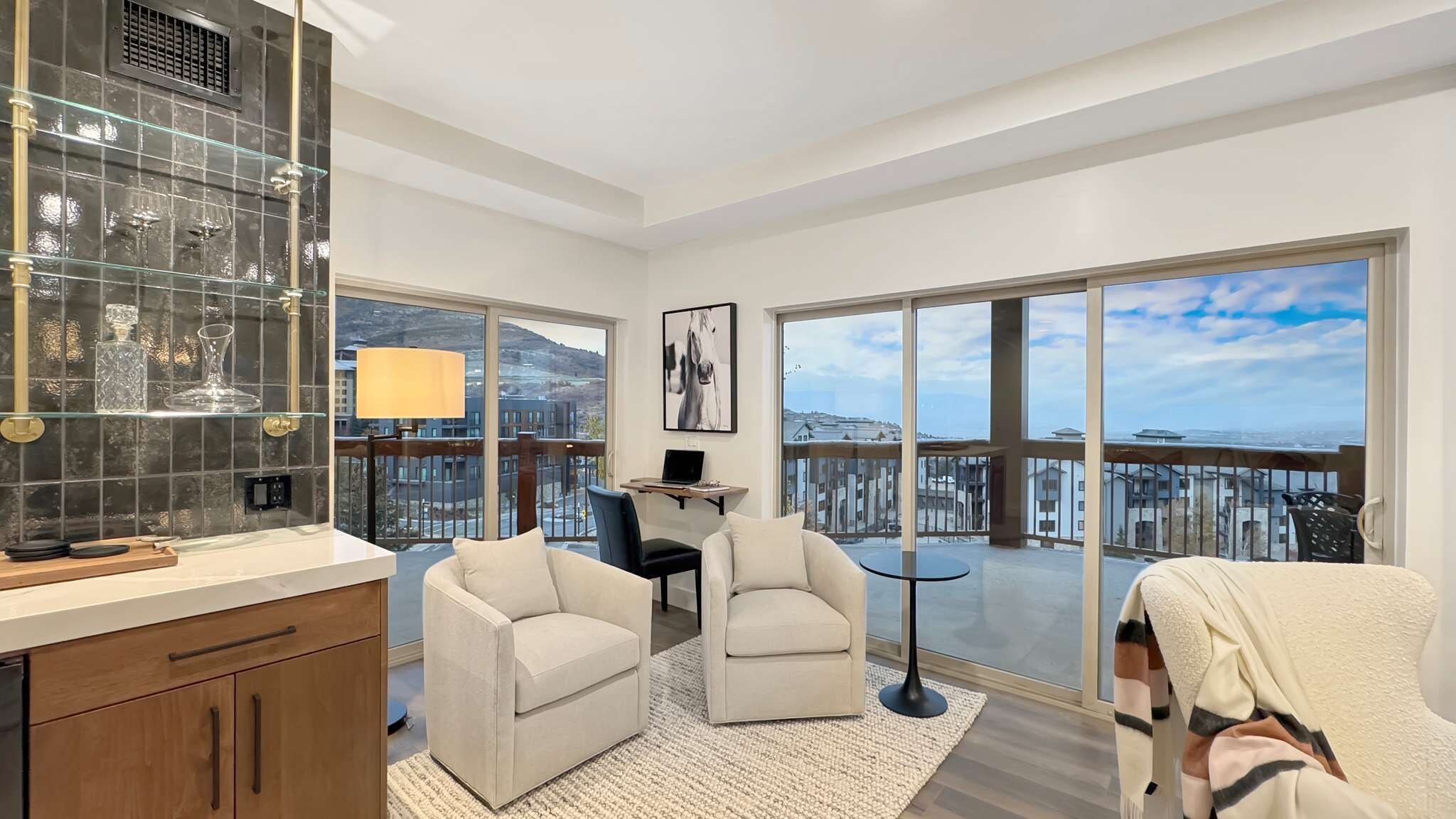 A spacious balcony with a city view, a modern kitchen with a glass backsplash, and two seating areas with a laptop on a small table.
