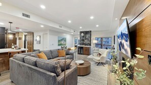 A modern living room with a grey sofa, a round coffee table, and a flat-screen TV mounted on the wall. - Renovated Presidential Suite•3 Fireplaces•Private Hot Tub w/Views•Resort Ameniti (Park City)