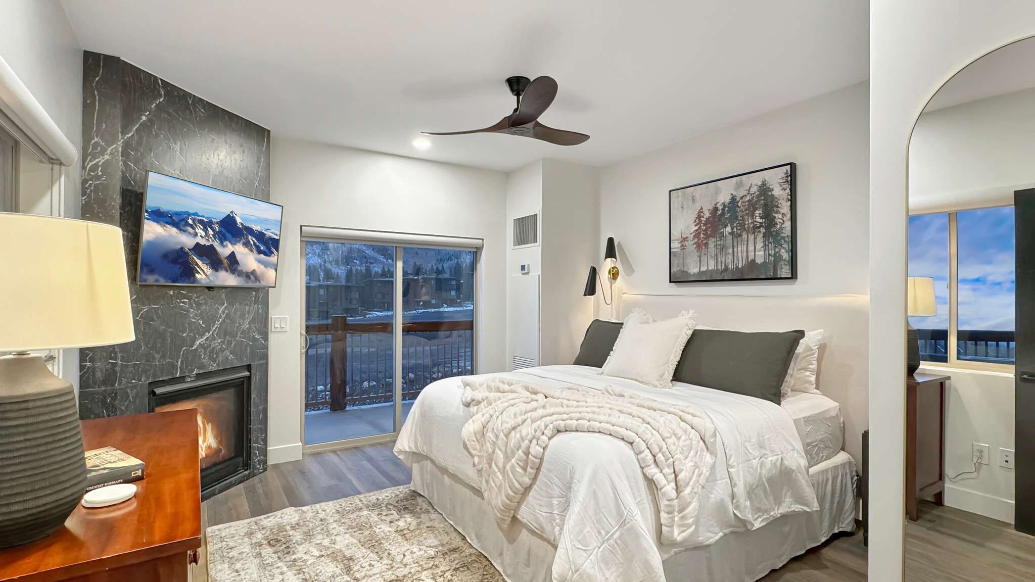 A bedroom with a bed, a fireplace, a ceiling fan, and a view of a snowy landscape through a sliding door.