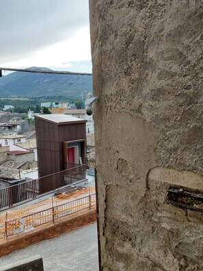 Visão de um prédio com uma câmera de vigilância, uma pequena construção com uma porta vermelha e um canteiro de obras com cercas laranjas.