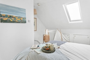 Un dormitorio con cama, ventana, un cuadro y una mesita de noche con objetos.