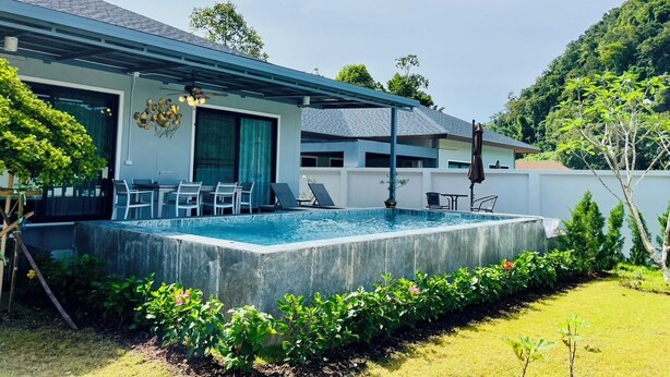 Ein modernes Haus mit Swimmingpool, Sitzgelegenheiten im Freien und üppigem Grün.