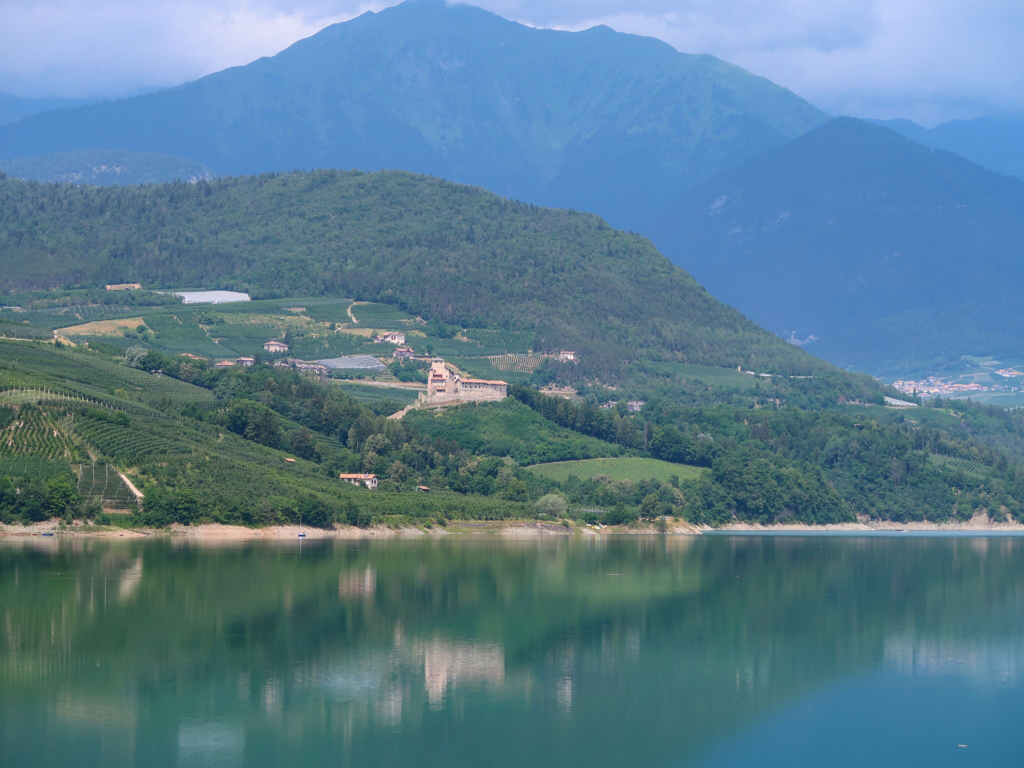 A mountainous landscape with a lake, terraced vineyards, and a castle-like structure.