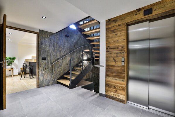 A modern interior with a staircase, a wooden wall, and a metallic elevator.