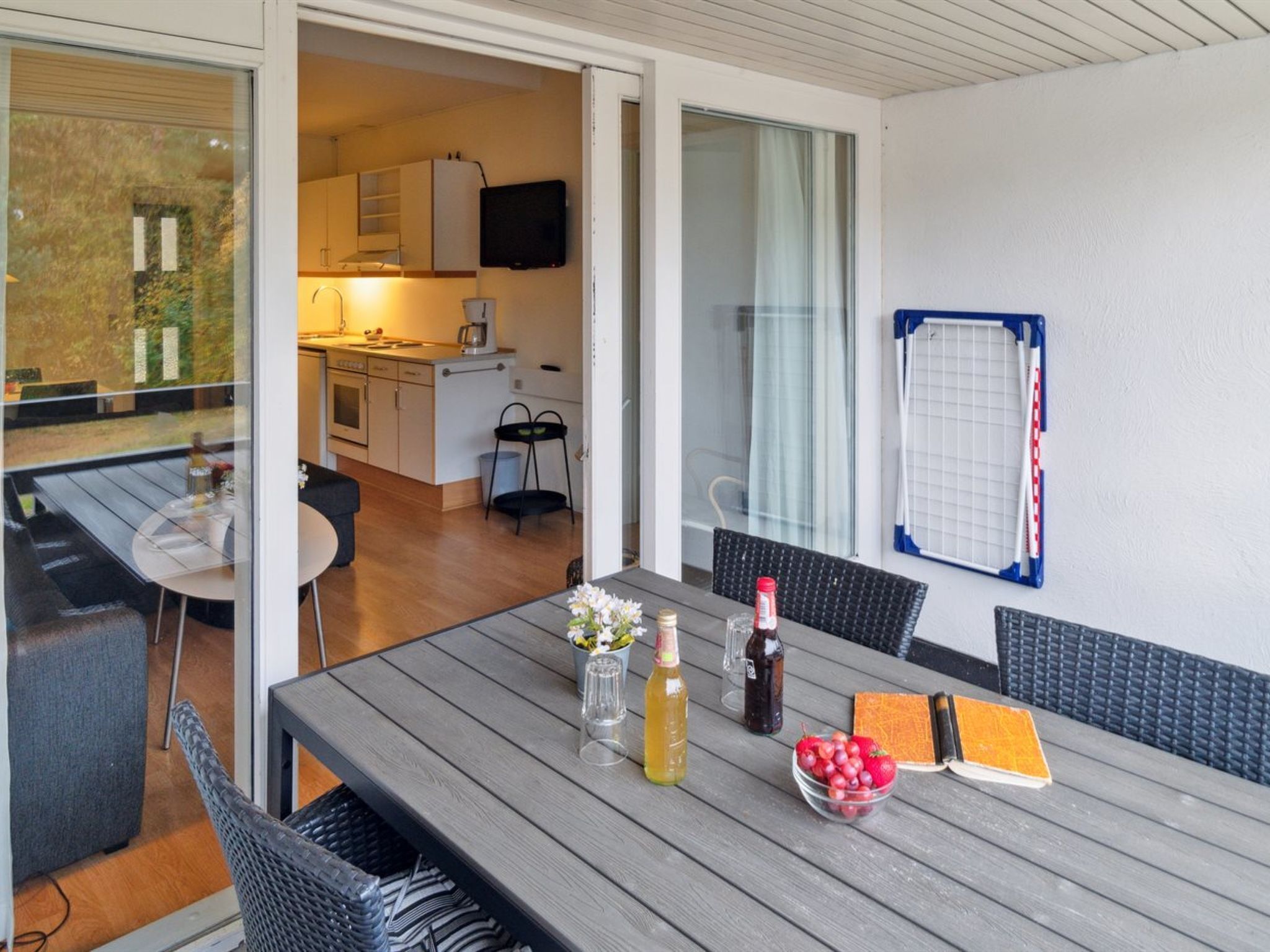 Eine moderne Küche mit weißen Schränken und einem eingebauten Ofen, ein Essbereich mit Holztisch und -stühlen sowie ein Blick ins Freie durch eine Glastür.