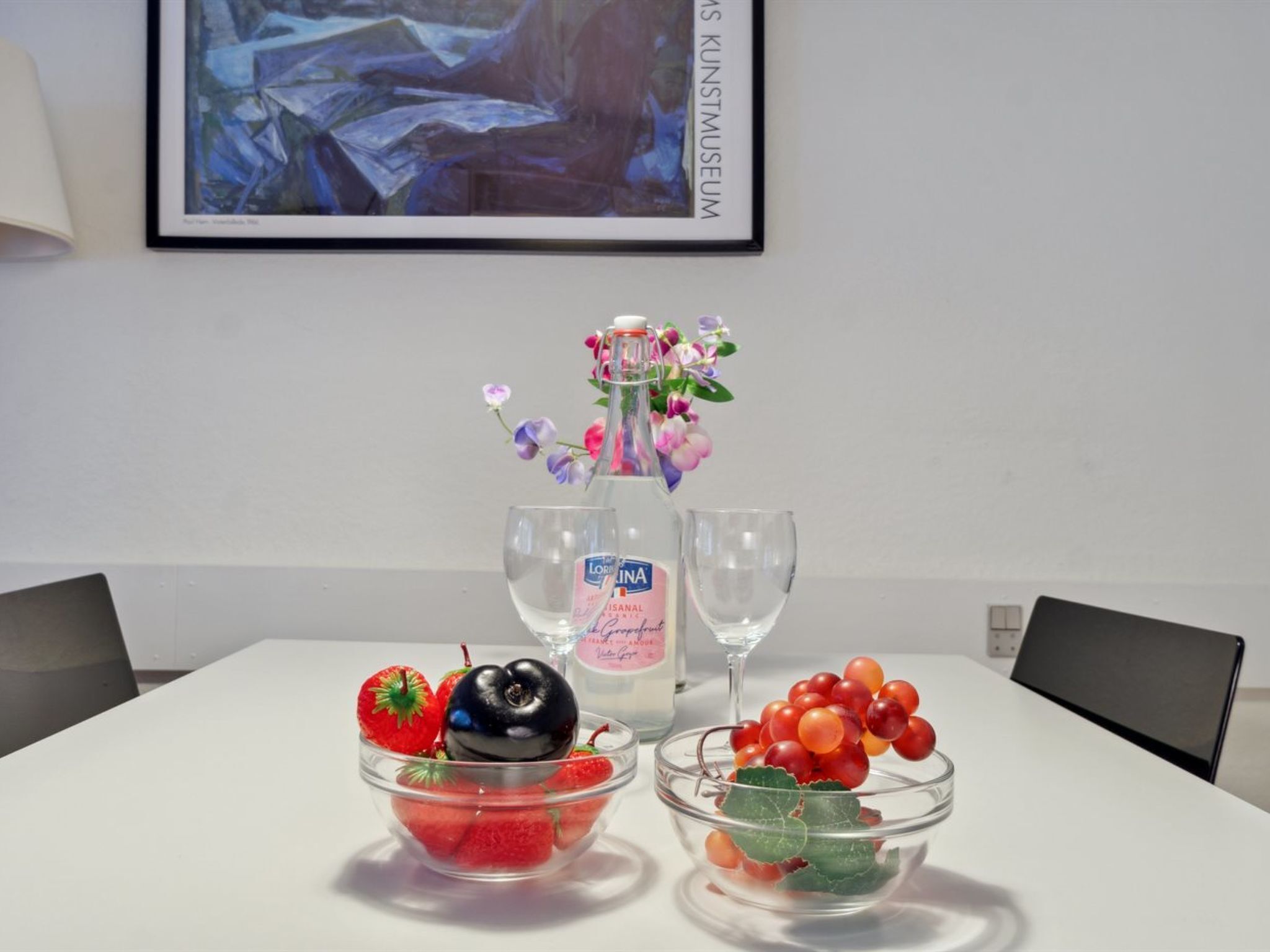 A table with a bottle of Lorrinalis, two glasses, and bowls of strawberries and grapes.