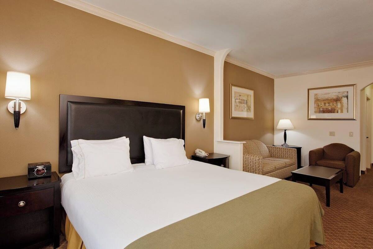 A hotel room with a large bed, two bedside tables, a chair, a small table, and two wall-mounted lamps.