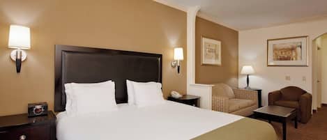 A hotel room with a large bed, two bedside tables, a chair, a small table, and two wall-mounted lamps.
