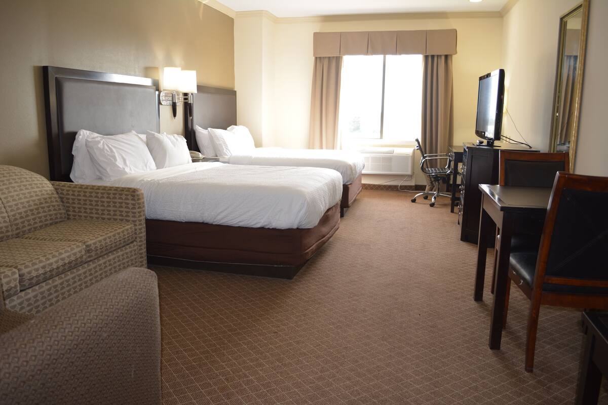 A hotel room with two beds, a desk, a chair, and a TV.