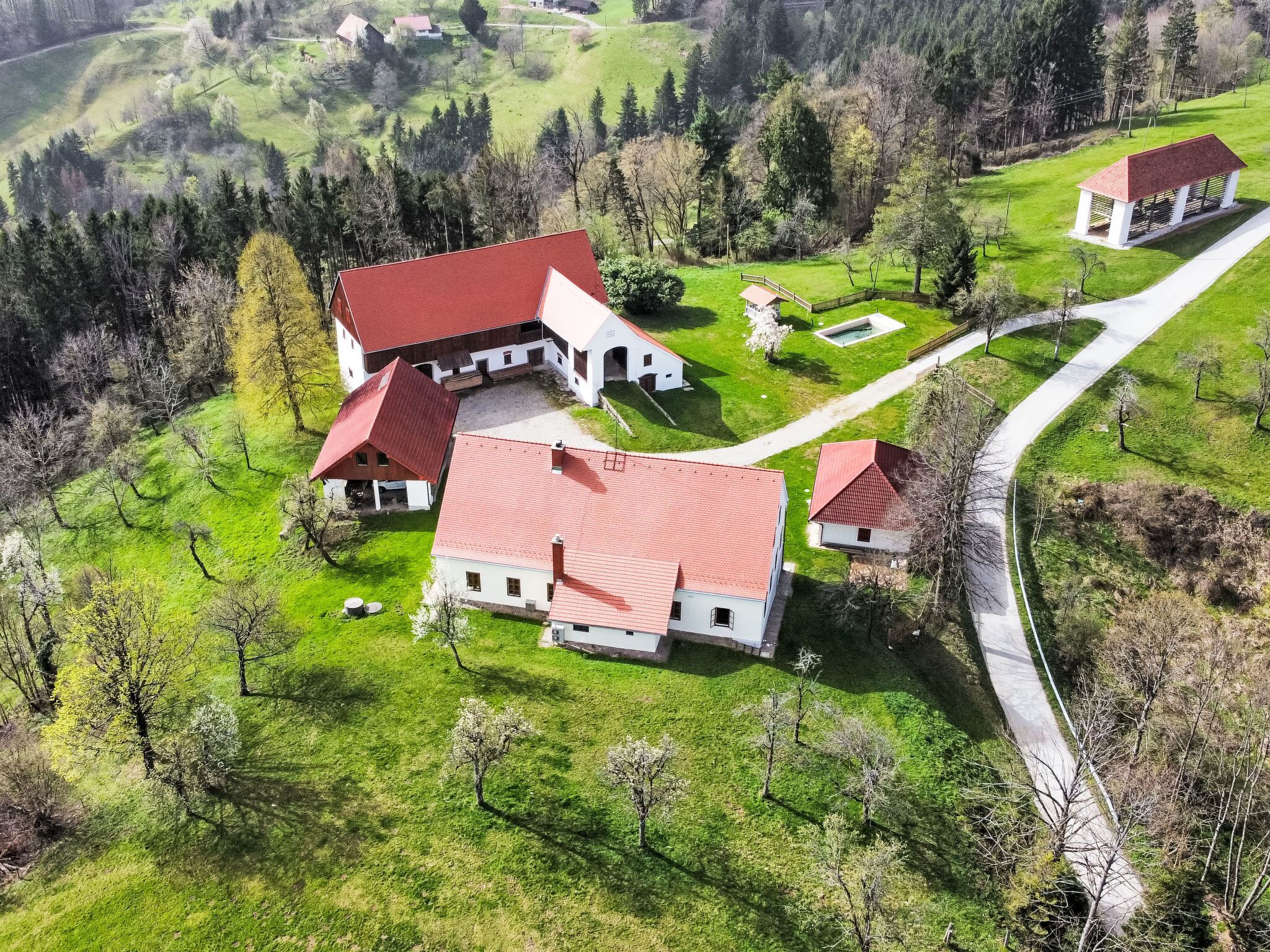 A large, red-roofed building complex with multiple structures, surrounded by lush green fields and trees.