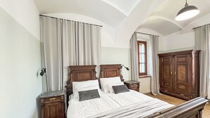Un dormitorio con una cama grande, cabecera de madera, dos mesitas de noche, un armario y una ventana con cortinas.