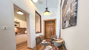 Una cocina compacta con armarios de madera, microondas y un lavamanos. Una zona de comedor con mesa y sillas de madera es contigua, con un cuadro en la pared.