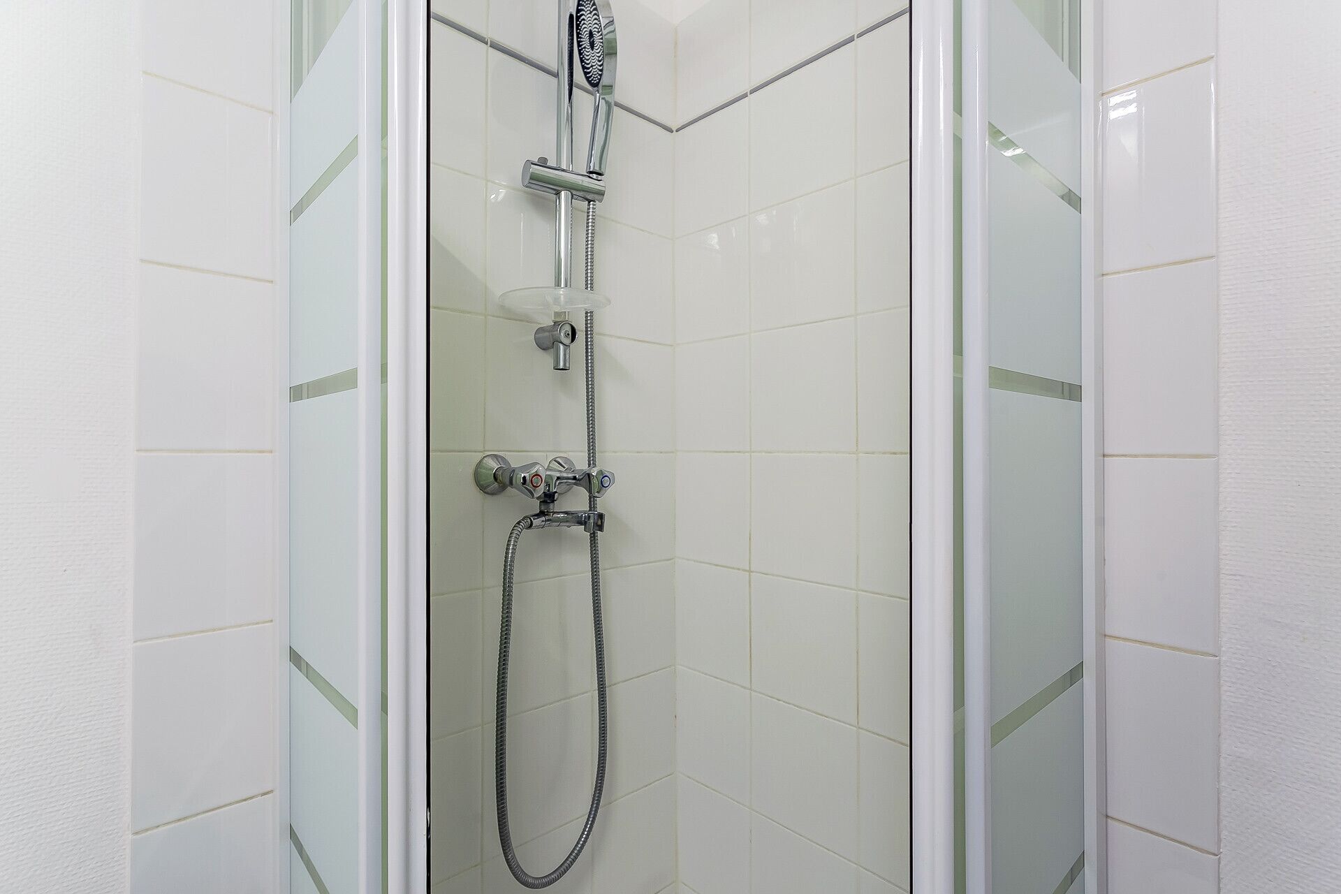 Ducha con cerramiento de vidrio, cabezal de ducha de mano, grifo empotrado y manguera flexible.