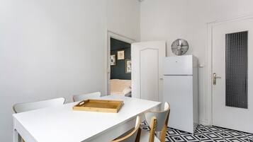 Una cocina compacta con una mesa blanca, dos sillas, un refrigerador y un piso con diseño.