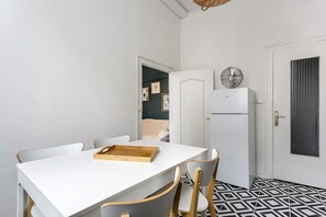 Eine kleine Küche mit einem weißen Tisch, zwei Stühlen, einem Kühlschrank und einem Musterfußboden.