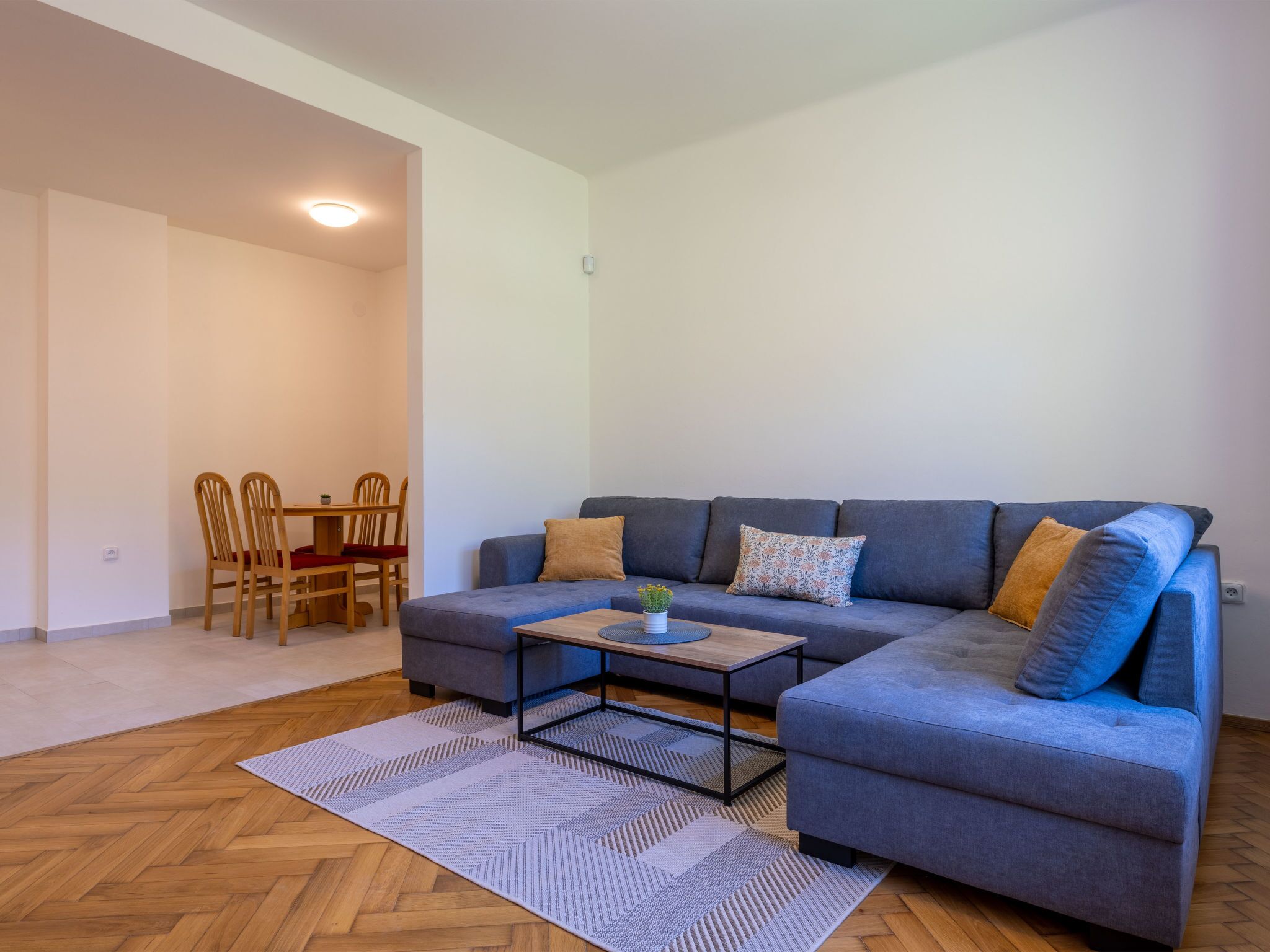 Un salon moderne avec un canapé d’angle gris, une table basse et un coin repas comprenant des chaises en bois et une petite table.