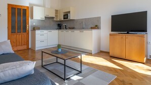 Una cocina moderna con armarios blancos, microondas y cafetera. Hay un mueble de madera con un televisor de pantalla plana encima.