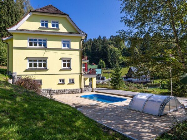 A two-story yellow house with a swimming pool and a greenhouse.