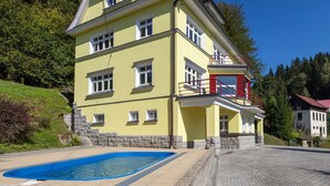 Un edificio de dos plantas con piscina, escalones de piedra y una zona pavimentada.
