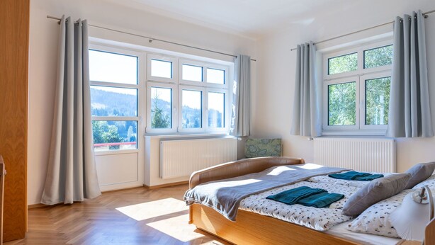 Un dormitorio con cama de madera, ventanas amplias y vistas al exterior.