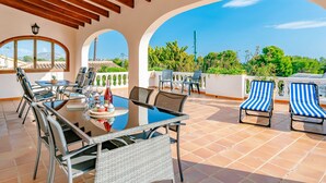 Un patio al aire libre con una mesa dispuesta para comer, rodeado de sillas y vistas al paisaje.