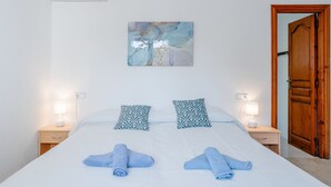 Una cama bien hecha con dos toallas enrolladas, un aire acondicionado de pared y un cuadro encima.