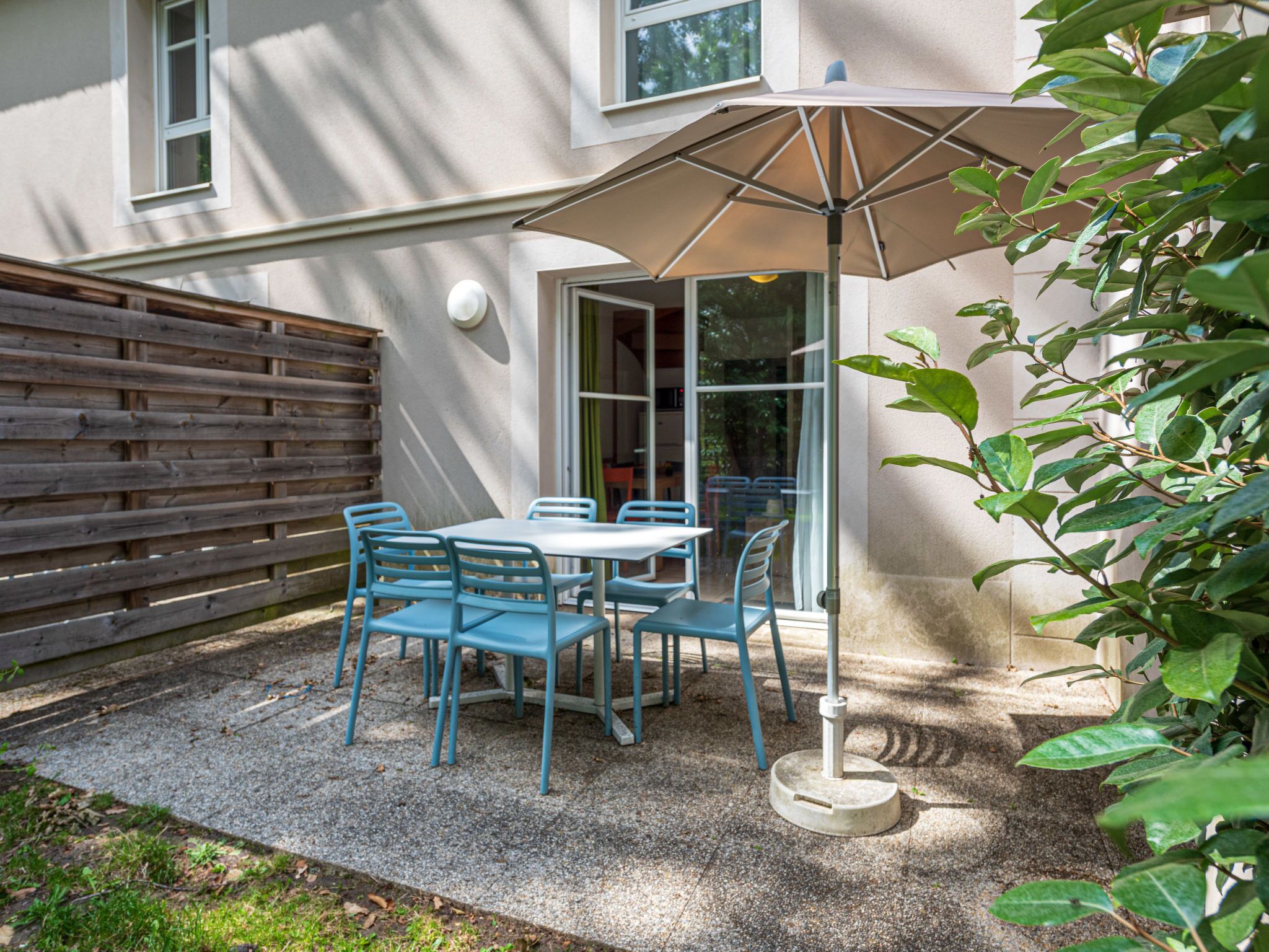 A patio with a table and chairs, a wooden fence, and a building in the background.