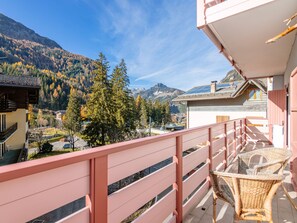 Ein Balkon mit einem Korbstuhl, einem pinkfarbenen Geländer und Blick auf eine Berglandschaft.