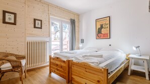 Un dormitorio con una cama de madera, una silla de mimbre, una mesita de noche con lámpara y un cartel en la pared.