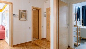 Un pasillo con piso de madera, un cuadro enmarcado en la pared y una puerta que da a un baño con espejo y estantes.