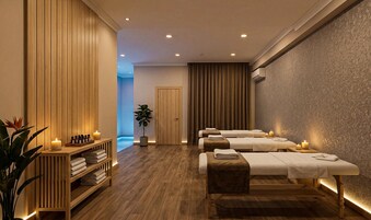 Un cuarto de spa con pisos de madera, tres mesas de masaje, un estante de madera con toallas, una planta en maceta y una puerta que da a un área iluminada en azul.
