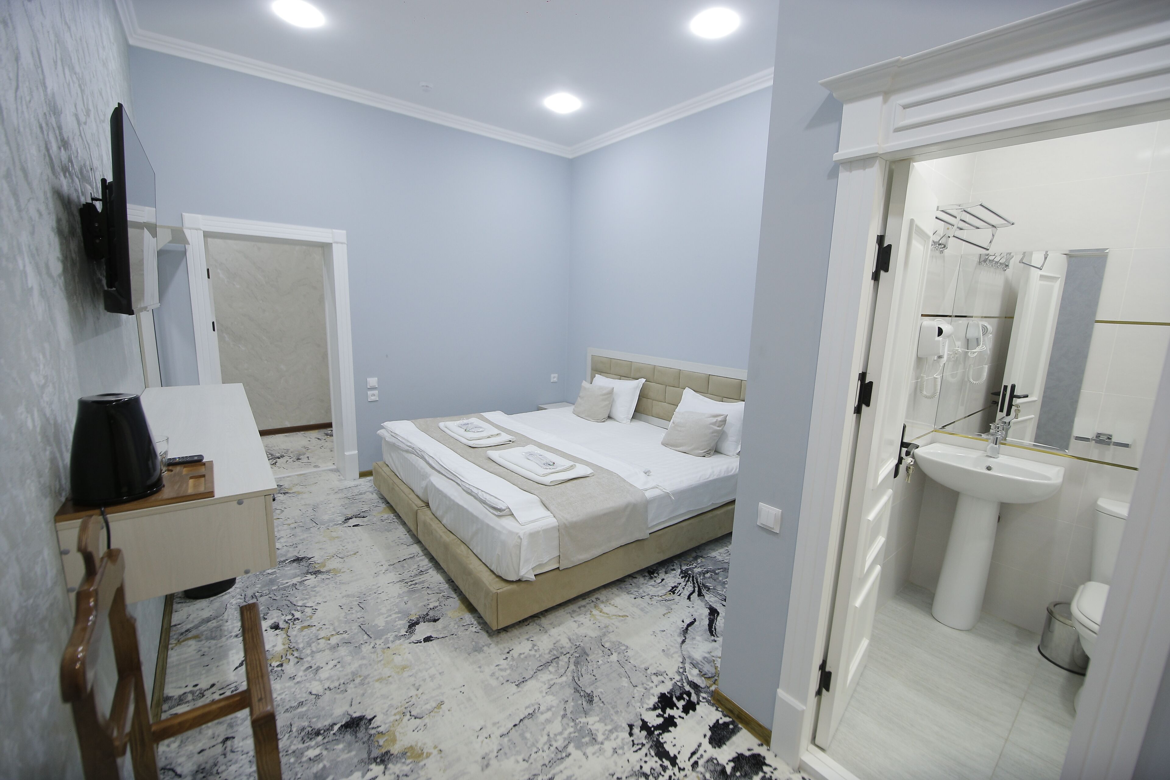 A bedroom with a bed, bedside table, and a bathroom with a sink and mirror.