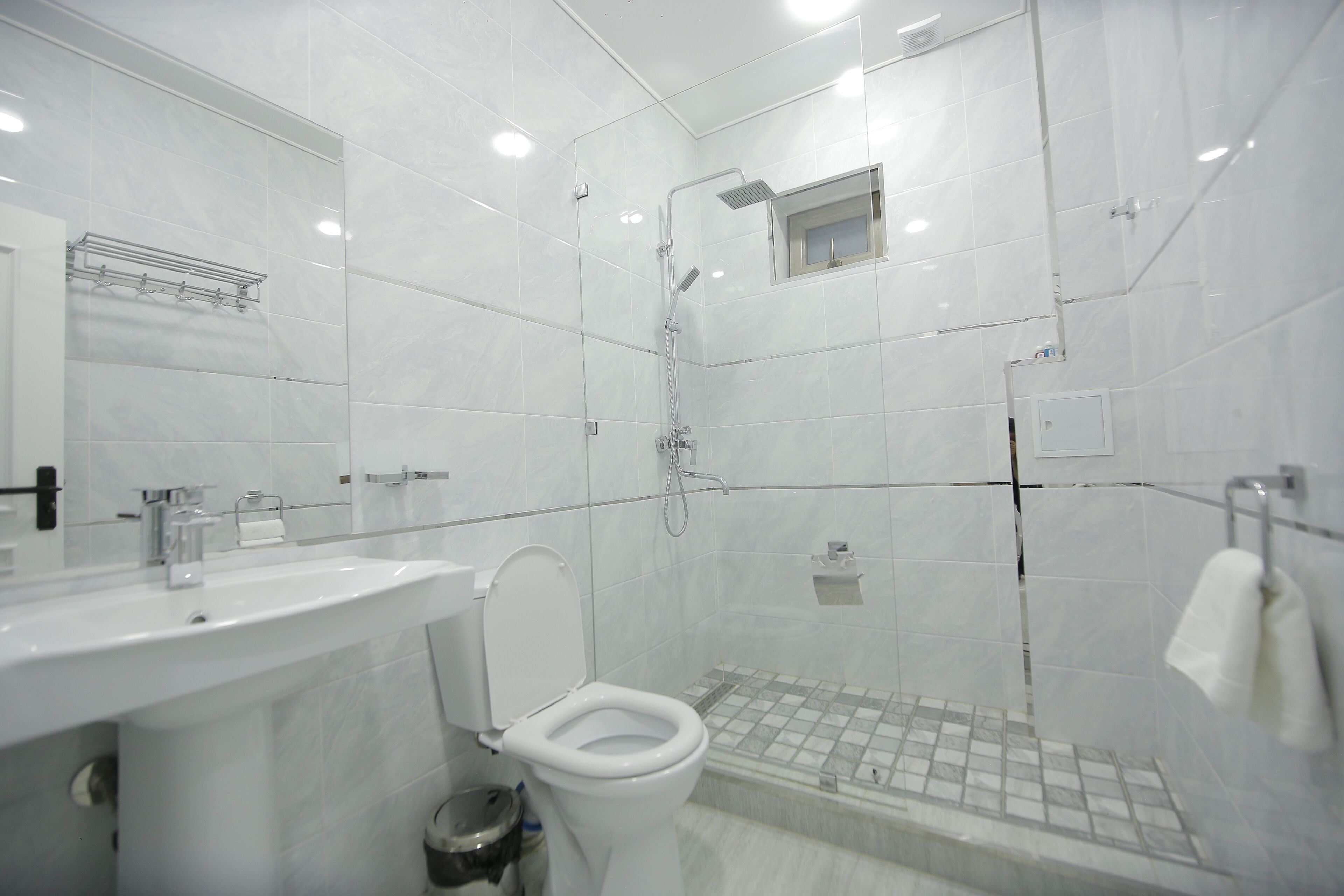 Un baño moderno con lavamanos, inodoro y zona de ducha blancos.