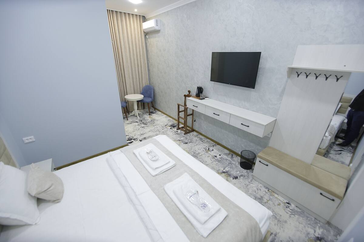 A hotel room with a bed, a desk, a chair, a TV, and a wardrobe.