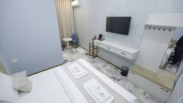 A hotel room with a bed, a desk, a chair, a TV, and a wardrobe.