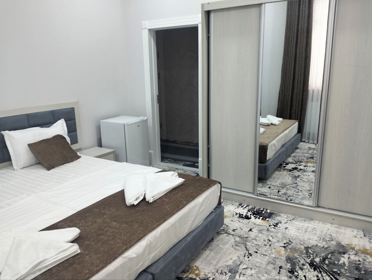 A hotel room with a bed, a bedside table, a wardrobe, and a mirror.