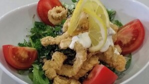 A bowl of salad with lettuce, tomatoes, and fried seafood, topped with lemon slices and a creamy dressing.