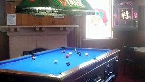 A pool table with balls, a television above it, and a neon sign.