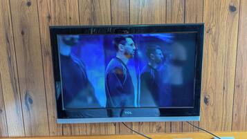 Uma TV TCL fixada numa parede de madeira, com uma tomada e interruptor visíveis abaixo.