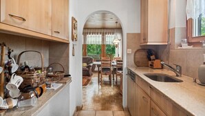 A narrow kitchen with wooden cabinets, a sink, and a dining area with a table and chairs. - Vacation home with parking lot Pet-friendly in the ski area (Wildhaus-Alt Sankt Johann)