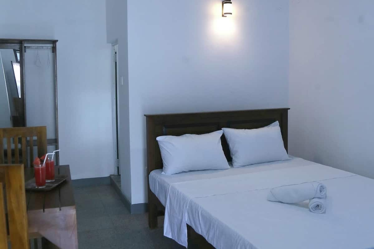 A bedroom with a bed, a ceiling fan, a bedside table with a mirror, and a wall-mounted light.
