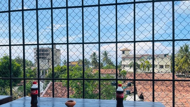 A balcony with a metal grid, two Coca-Cola bottles, and a small clay pot. - Emerald Coast Hotel Negombo (Kochchikade)
