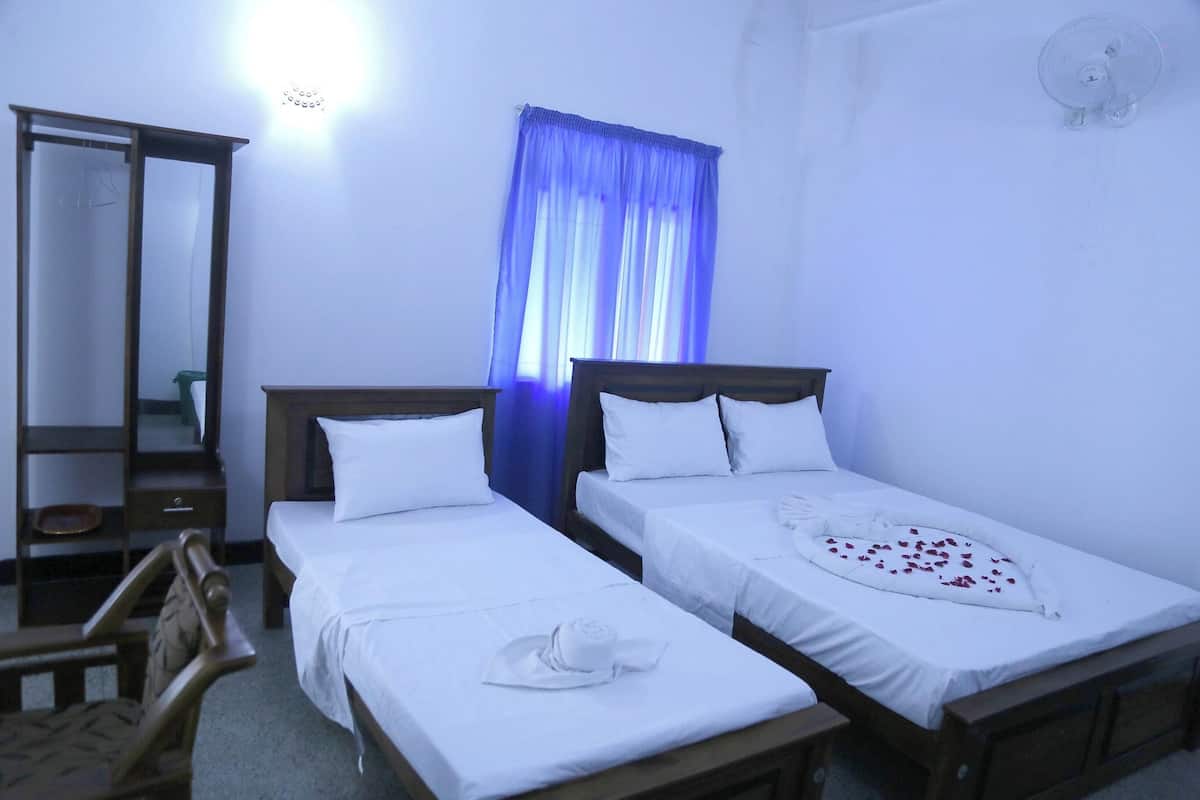 A hotel room with two single beds, a wooden wardrobe, a mirror, and a ceiling fan.